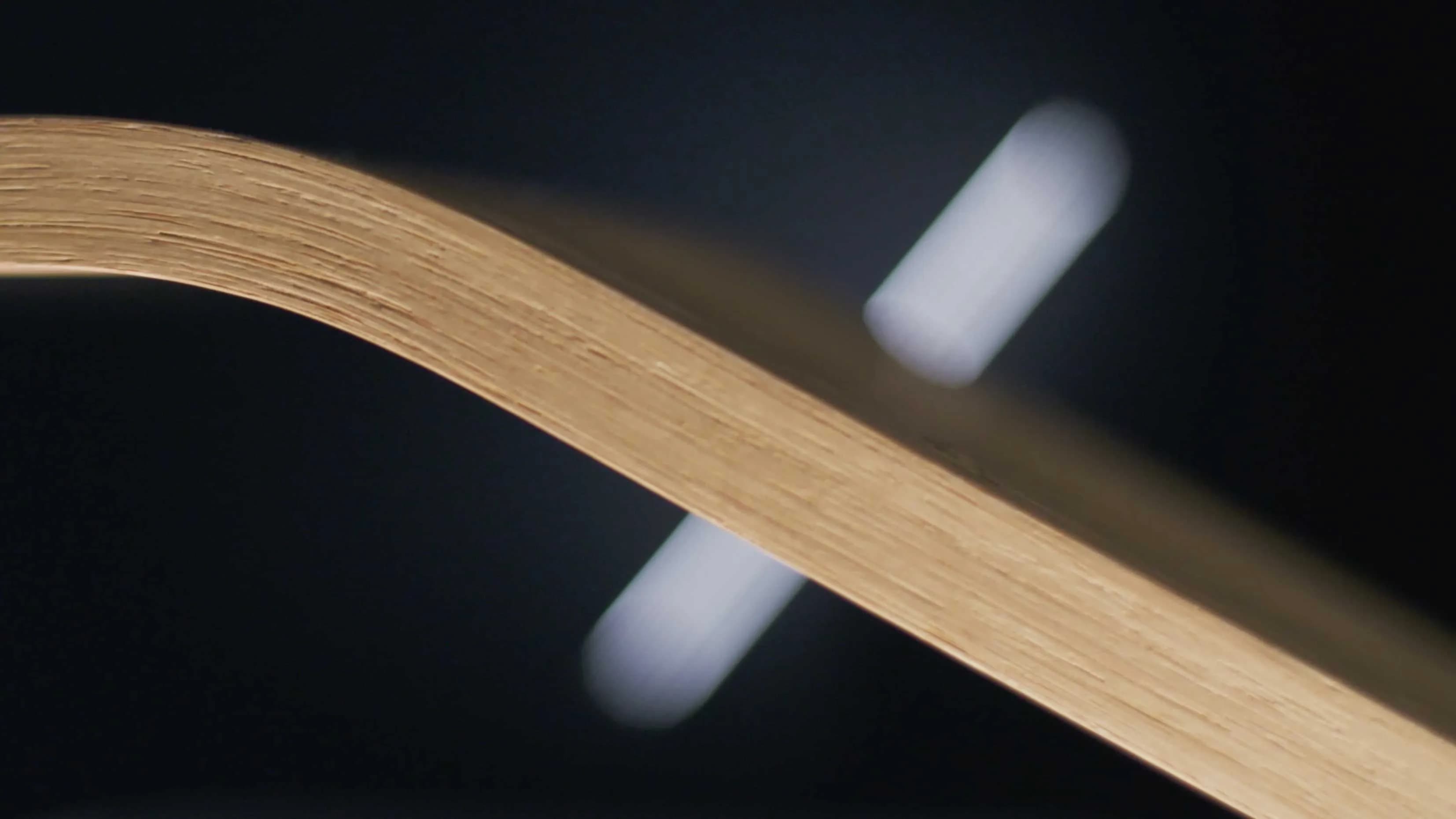 der Slash von F/List, geformt mit einem Lichtstab, gegen ein biegsames Holz im Vordergrund